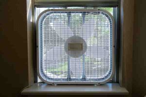 Fan placed on open window to improve airflow, control moisture, and reduce HVAC load.